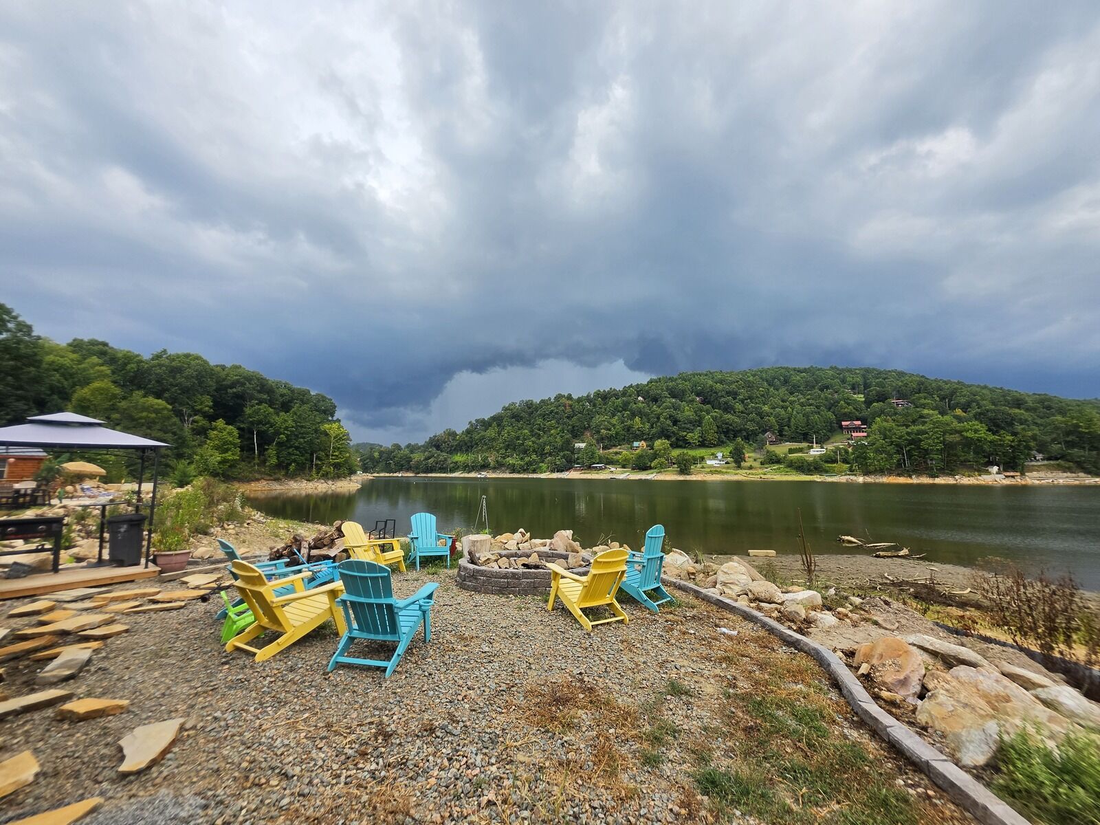 Storm clouds rolling over the lake behind the firepit and Adirondack chairs