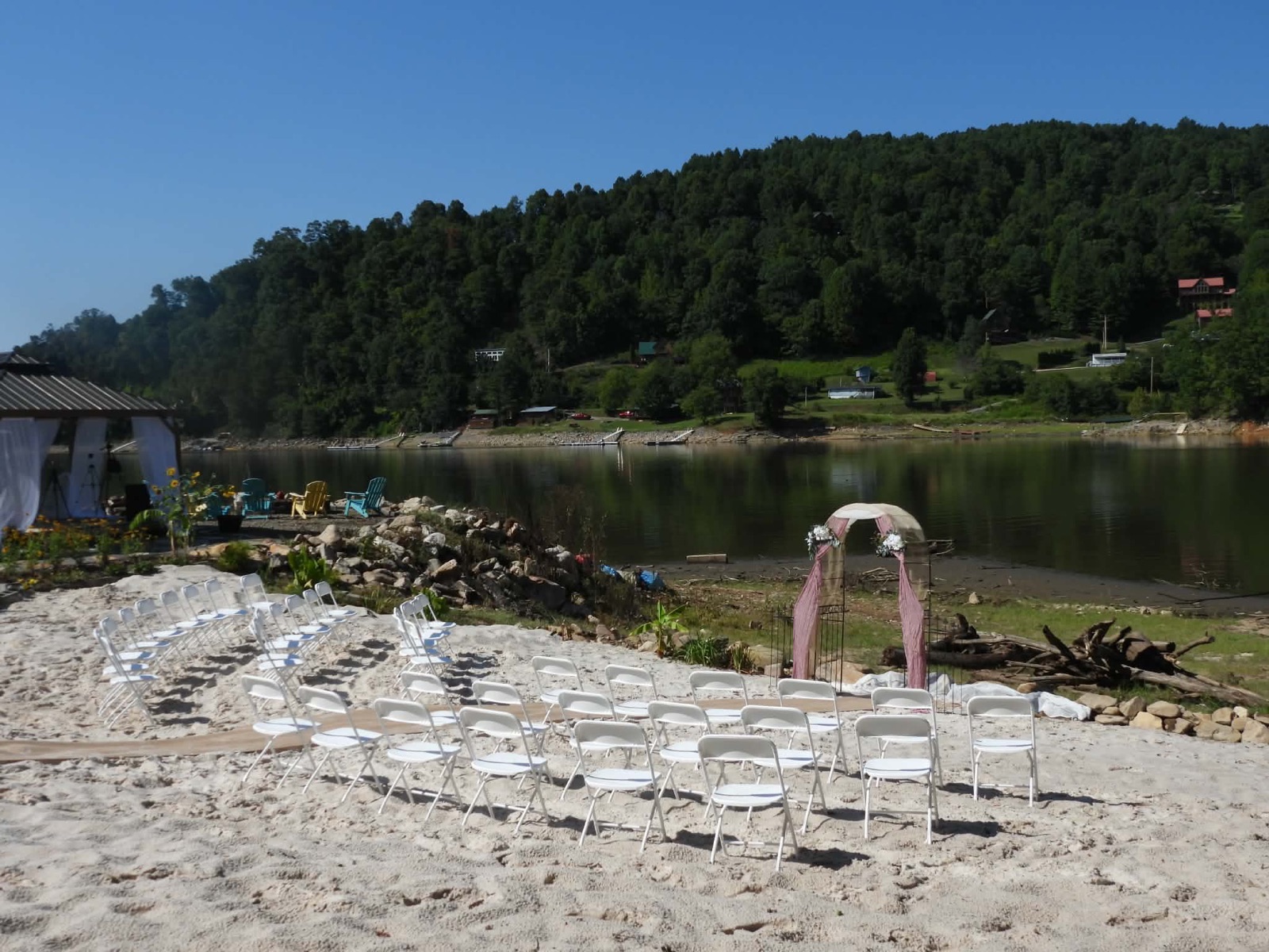 Rows of white chairs and a rose-draped arch set for a beach wedding at the water's edge
